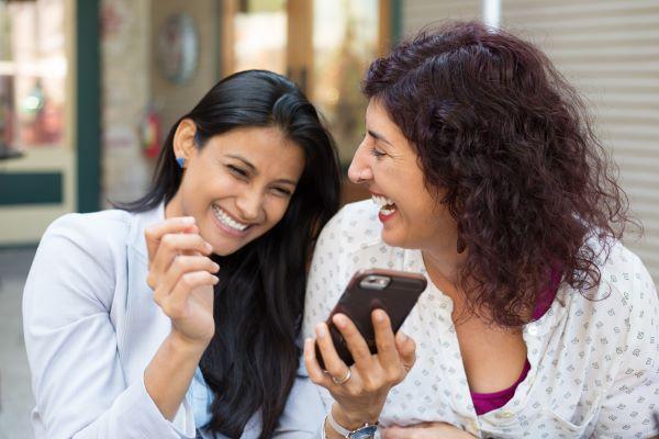 two women laughing at something on the phone