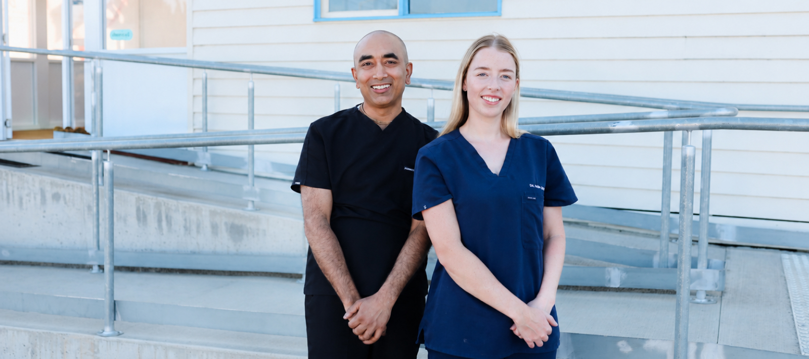 Whitehills Dental Practice | Three dental professionals standing confidently with arms crossed outside a white clinic building with blue trim, smiling at the camera.